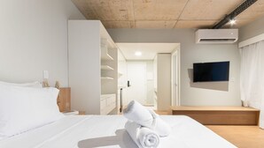 Une chambre d’hôtel avec un lit soigneusement fait, un téléviseur à écran plat fixé au mur et un banc en bois près de la fenêtre.