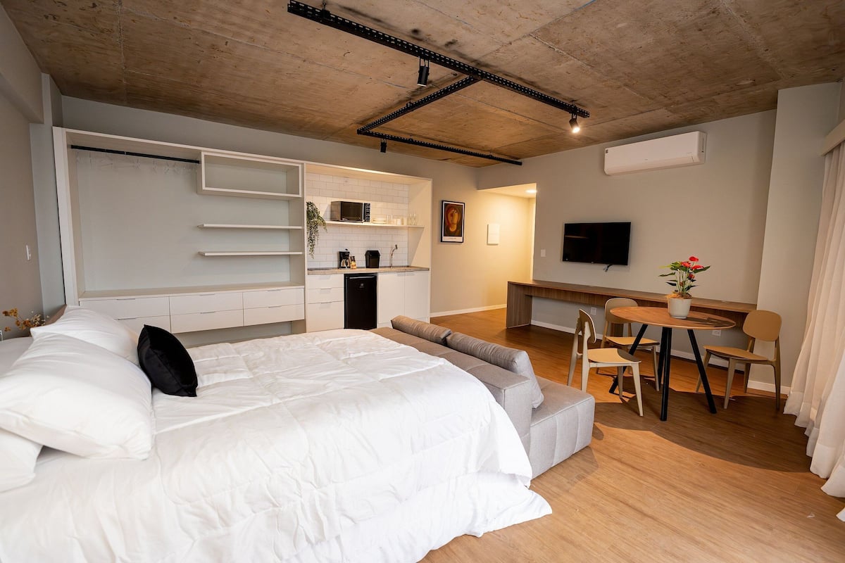 A modern bedroom with a bed, a sofa, a dining table, and a TV.