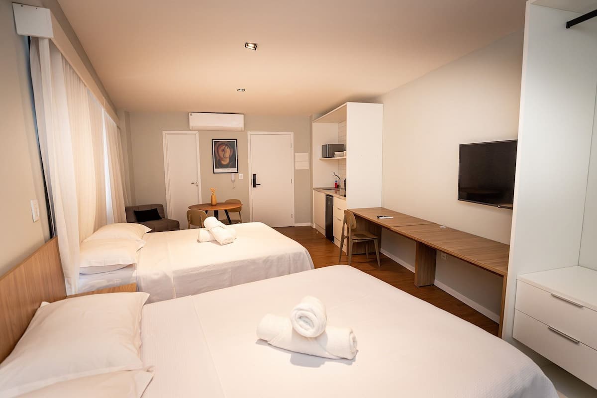 A hotel room with two beds, a desk, a chair, a TV, and a wardrobe.