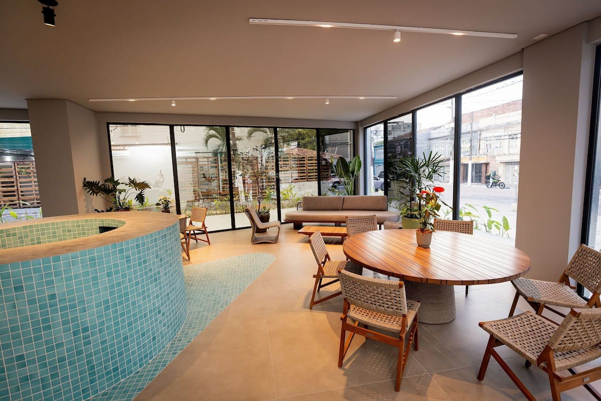 A modern indoor space with a pool, seating area, and large windows offering views of the street.