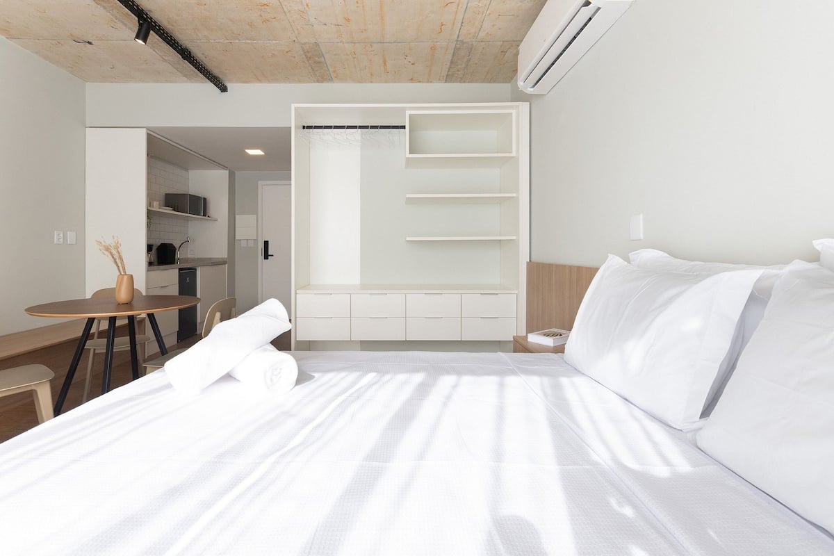 A modern hotel room with a large bed, a small desk, and a walk-in closet with shelves.