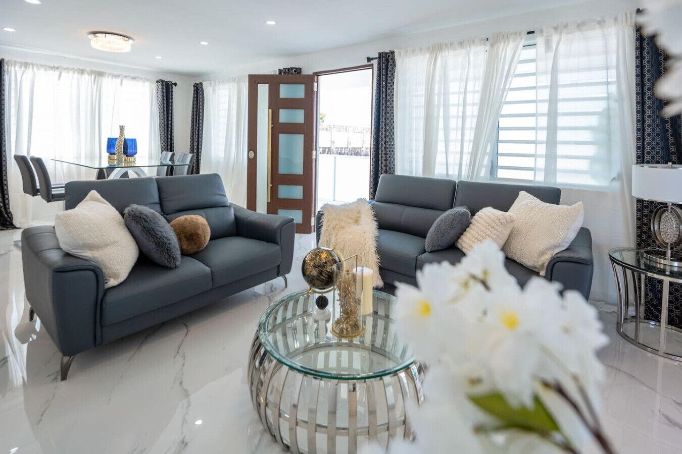 A modern living room with two grey sofas, a glass coffee table, and a door leading to a balcony.