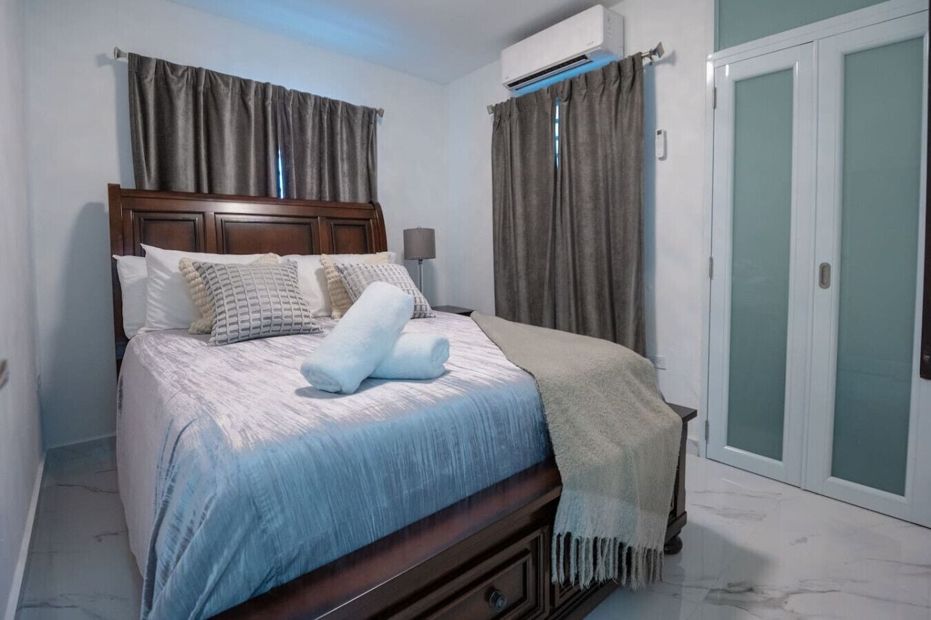 Een slaapkamer met een bed, nachtkastje, airconditioning en een deur met geëtste glaspanelen.