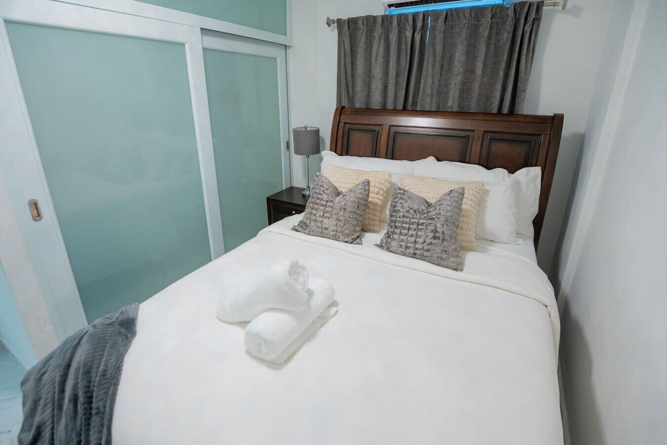 A neatly made bed with white linens, a folded towel, and patterned pillows.