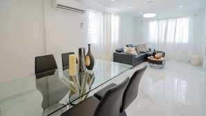 A modern living room with a glass dining table, grey sofa, and a large window with sheer curtains. - La Casa Blanca [Unit #1 Machete] (Carolina)