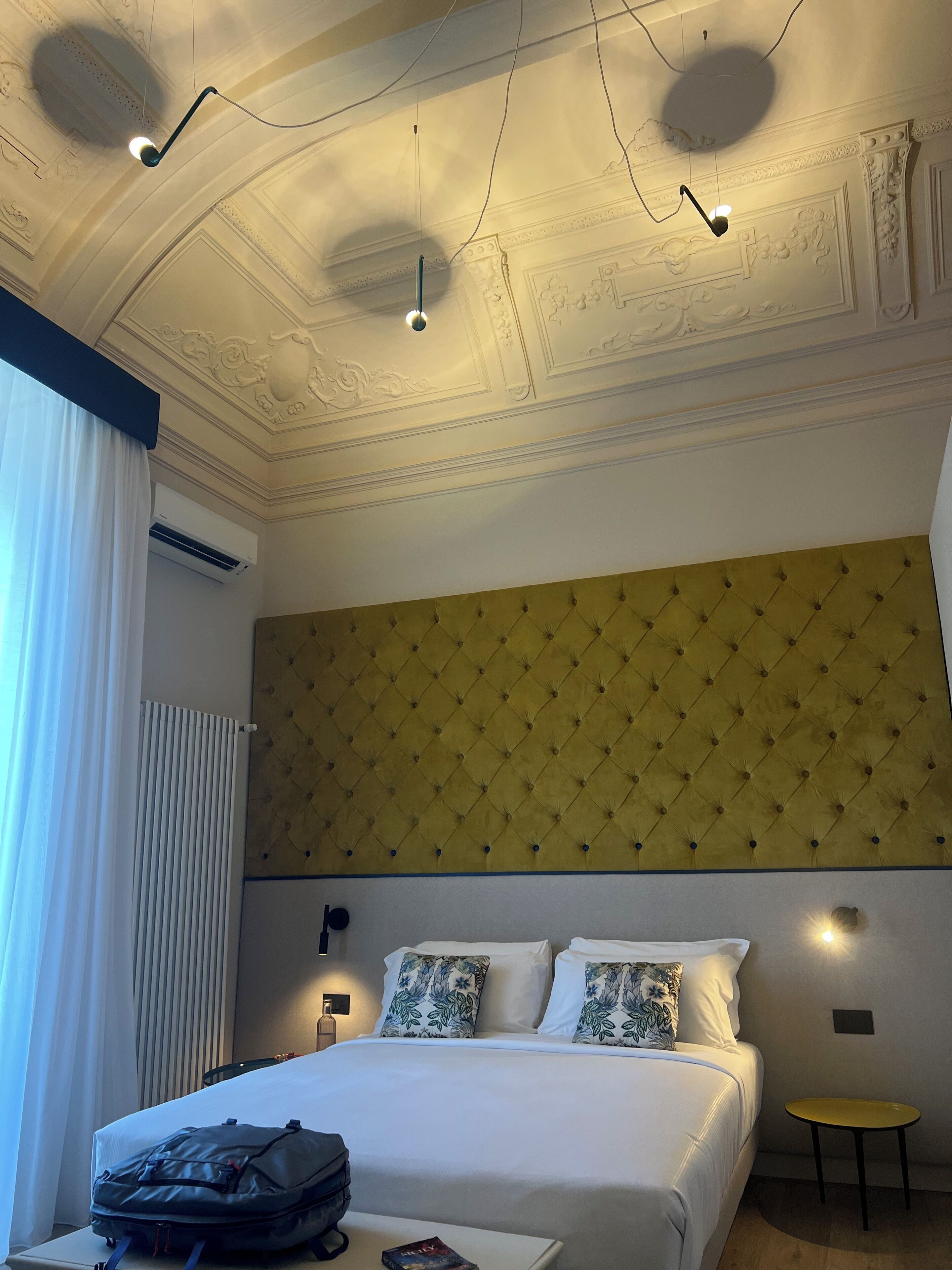 Habitació d'hotel amb llit, una taula de nit, una maleta i una taula petita groga.