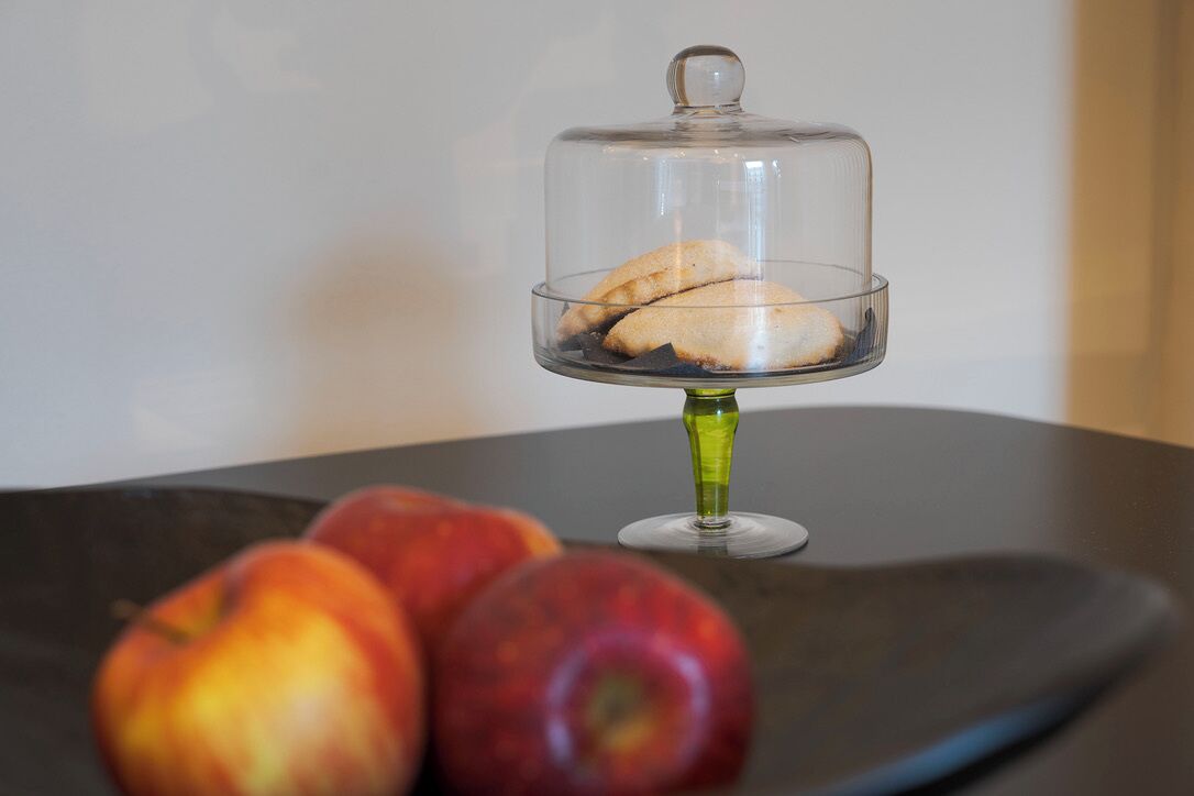 Copa de postre con una cubierta abovedada sobre una mesa, acompañada de tres manzanas.