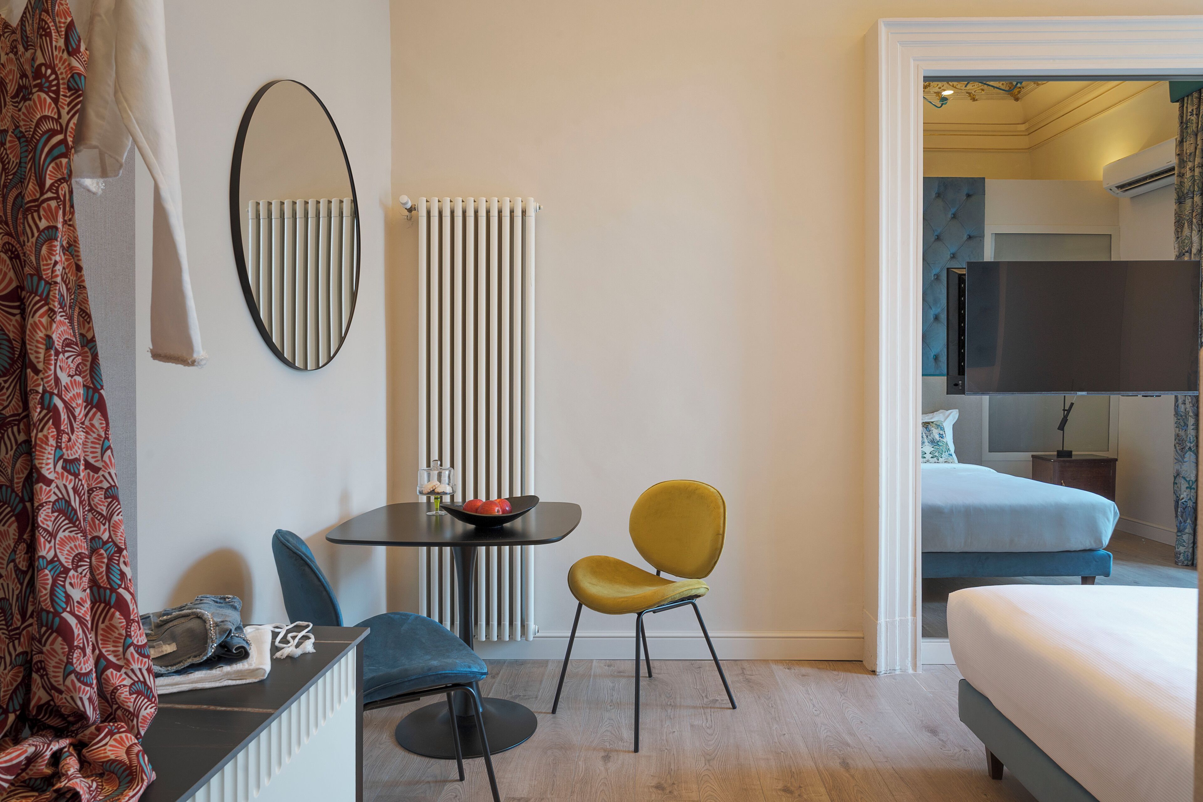Une chambre d’hôtel avec un lit, une télévision, une petite table sur laquelle se trouve un bol de fruits, deux chaises et un radiateur.