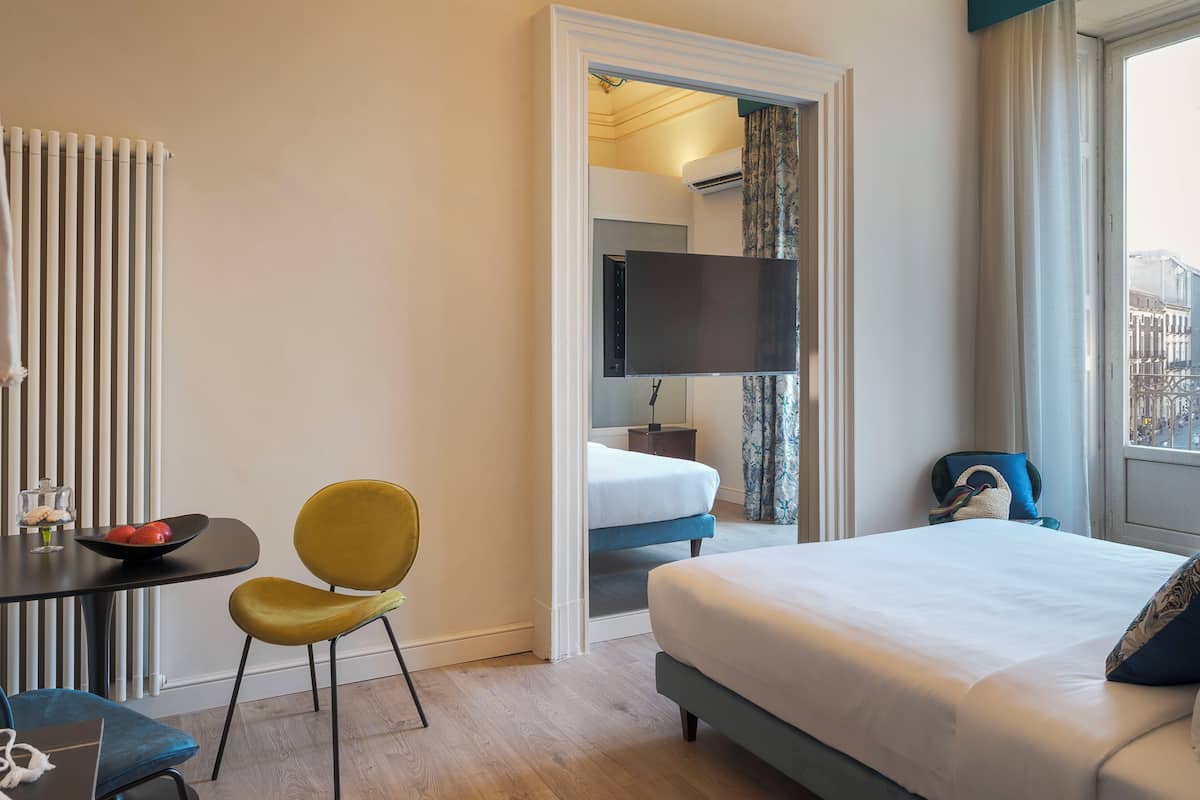Ein Hotelzimmer mit Bett, Schreibtisch mit Stuhl, Fernseher und Blick auf die Stadt durch das Fenster.