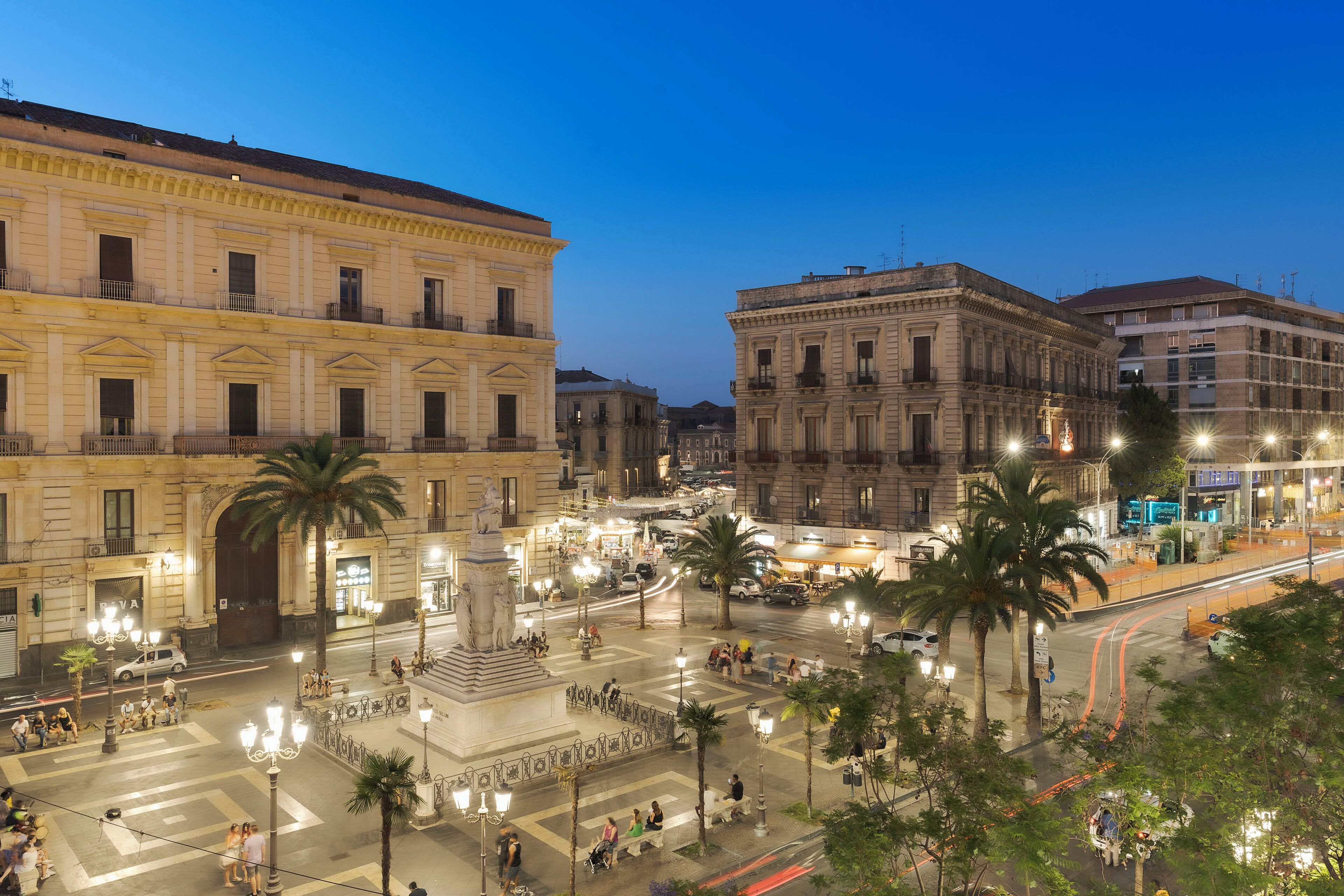Una plaza histórica con arquitectura clásica, un monumento central y palmeras.