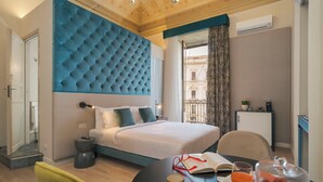 Een hotelkamer met een groot bed, een eettafel met een kop en een boek, en uitzicht op de stad door het raam.