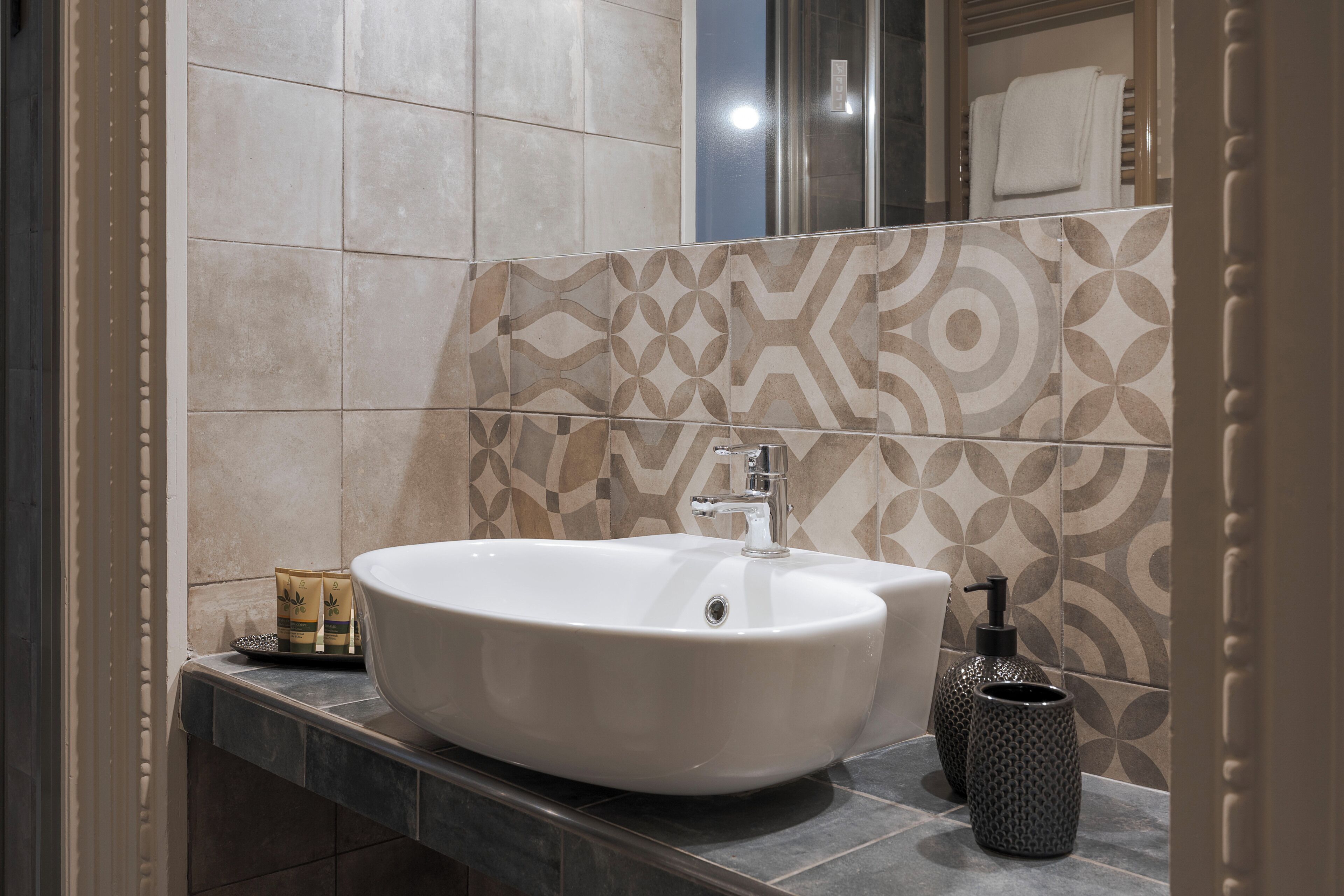 A bathroom with a large white sink, a mirror, and patterned tiles on the wall.