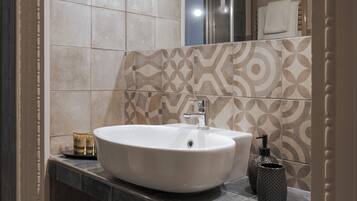 A bathroom with a large white sink, a mirror, and patterned tiles on the wall.