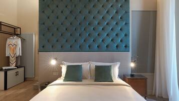 Ein Hotelzimmer mit einem großen, gepolsterten Kopfteil, einem Bett mit weißen Leinentüchern, zwei grünen Kissen, einem Nachttisch mit Lampe und einem Kleiderschrank mit Kleidung.