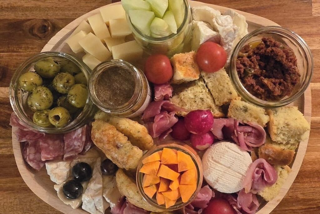 A charcuterie board with various cheeses, meats, olives, and pickled vegetables.