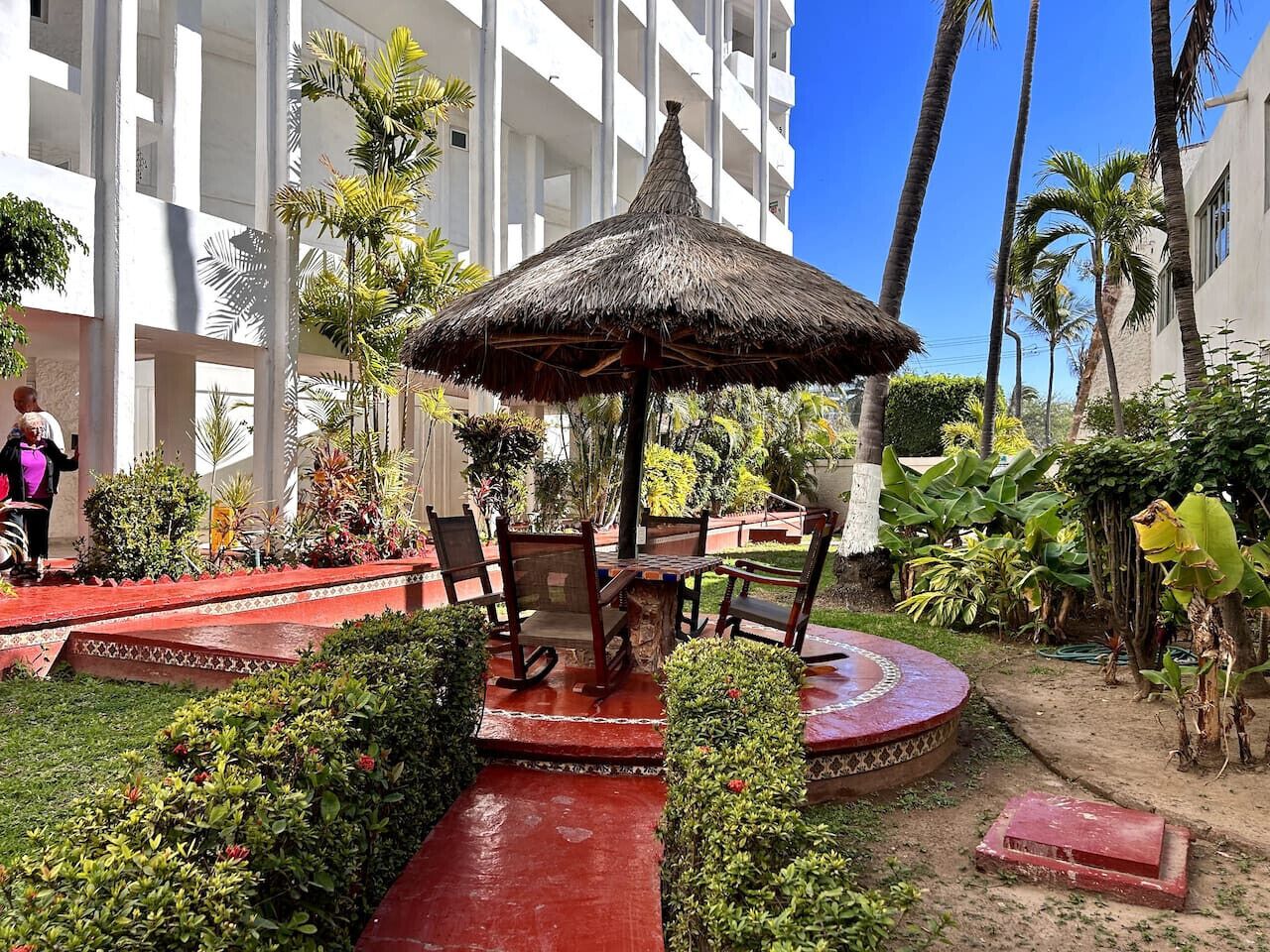 Un patio con un paraguas de paja, sillas de madera y un sendero rojo.