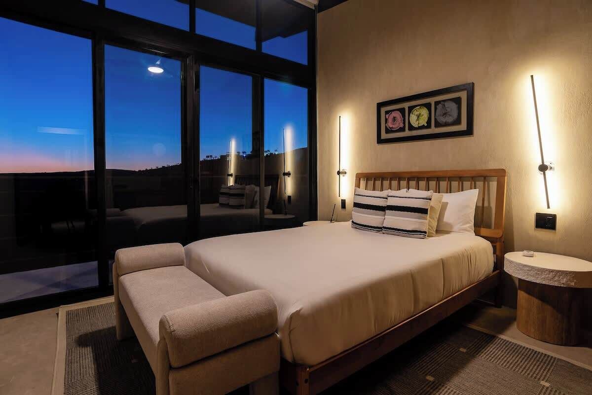 A bedroom with a large bed, a sofa, and a view of the sky through large windows.