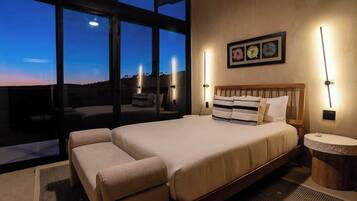 A bedroom with a large bed, a sofa, and a view of the sky through large windows.