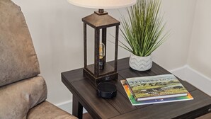 A dark wooden side table with a lamp, a potted plant, and a book.