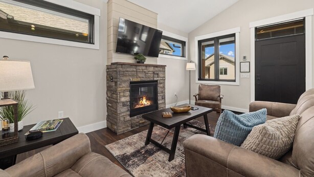 A living room with a stone fireplace, a flat-screen TV mounted above it, and a comfortable seating area with a sofa and armchairs.