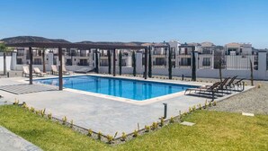 Una piscina con lettini, un pergolato e vista su edifici sullo sfondo.