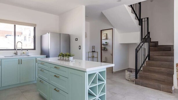 Una cucina moderna con pensili azzurri, un piano di lavoro bianco e una cantinetta a muro per vini.