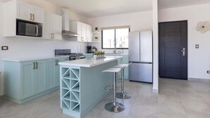 Una cucina moderna con mobili bianchi, un'isola centrale con sgabelli da bar, un forno a microonde, un piano cottura e un frigorifero.