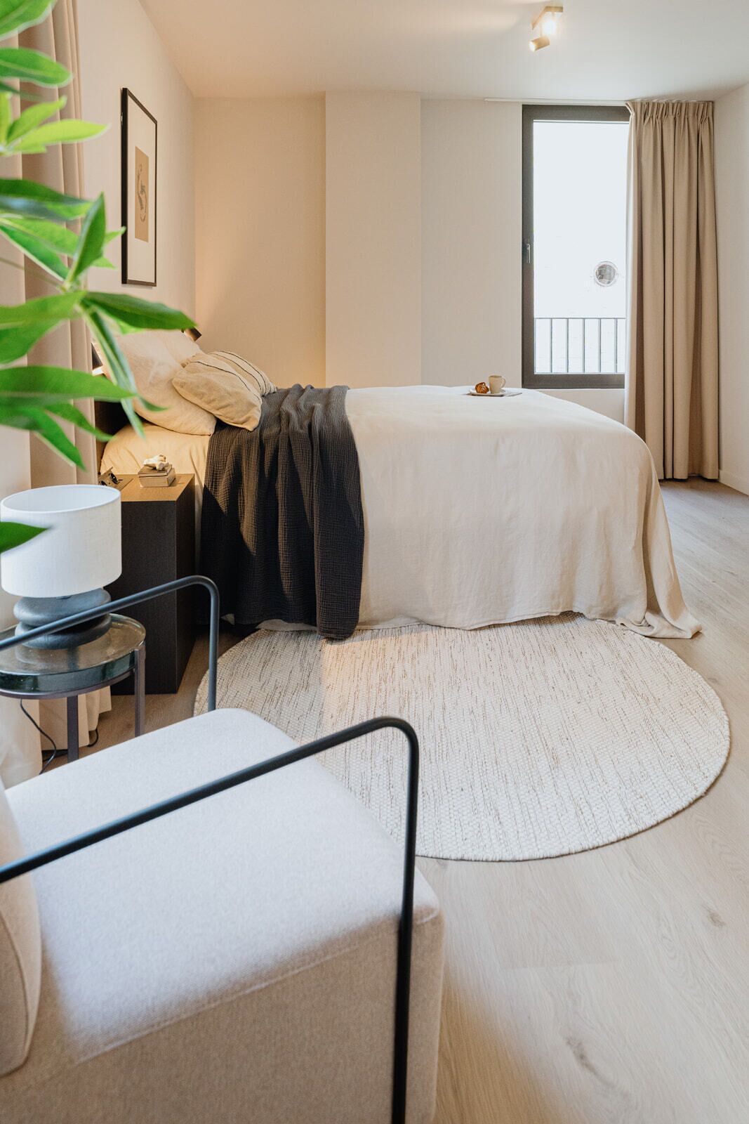 Ein modernes Schlafzimmer mit Bett, Nachttisch, Lampe und Blick ins Freie.