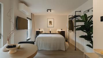Een moderne hotelkamer met een bed, nachtlampjes, een flatscreen televisie, een grote plant en een kleine tafel met een schaal olijven.