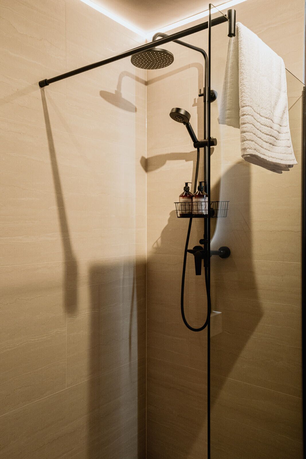 A modern shower enclosure with a handheld showerhead, a towel rack, and a soap dispenser.