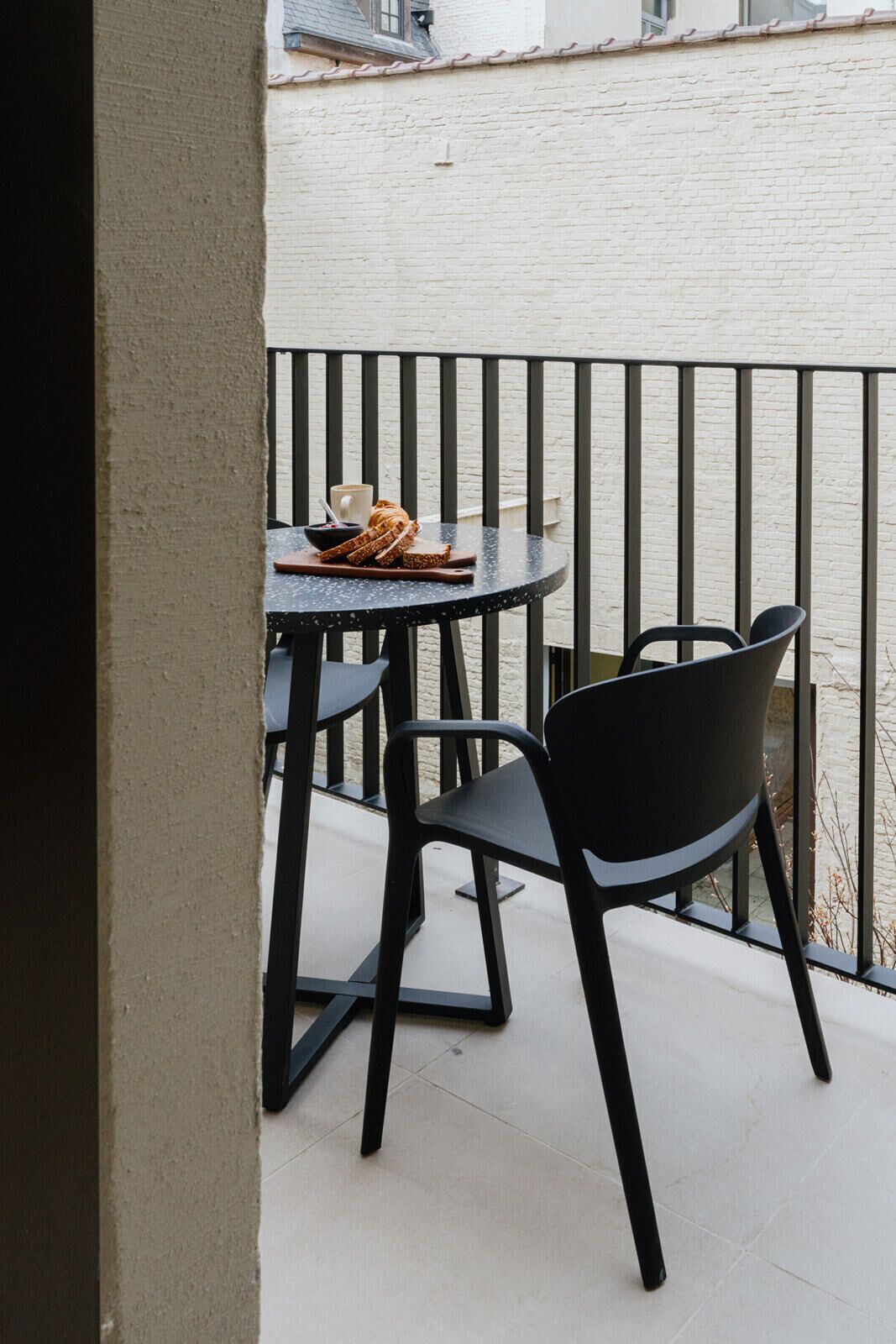 A balcony with a round table and two chairs, a loaf of bread, and a cup on the table.