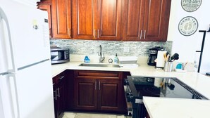 A compact kitchen with wooden cabinets, a microwave, a sink, and a stove. - Waikiki 2 bedrm Condo Canal View w/ Gated Parking (Honolulu)