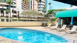 A swimming pool with lounge chairs and umbrellas, surrounded by a brick patio and palm trees. - Waikiki 2 bedrm Condo Canal View w/ Gated Parking (Honolulu)