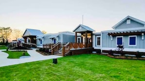 Una hilera de casas modernas, de un piso y estilo arquitectónico uniforme, con porche cubierto y césped cuidado.
