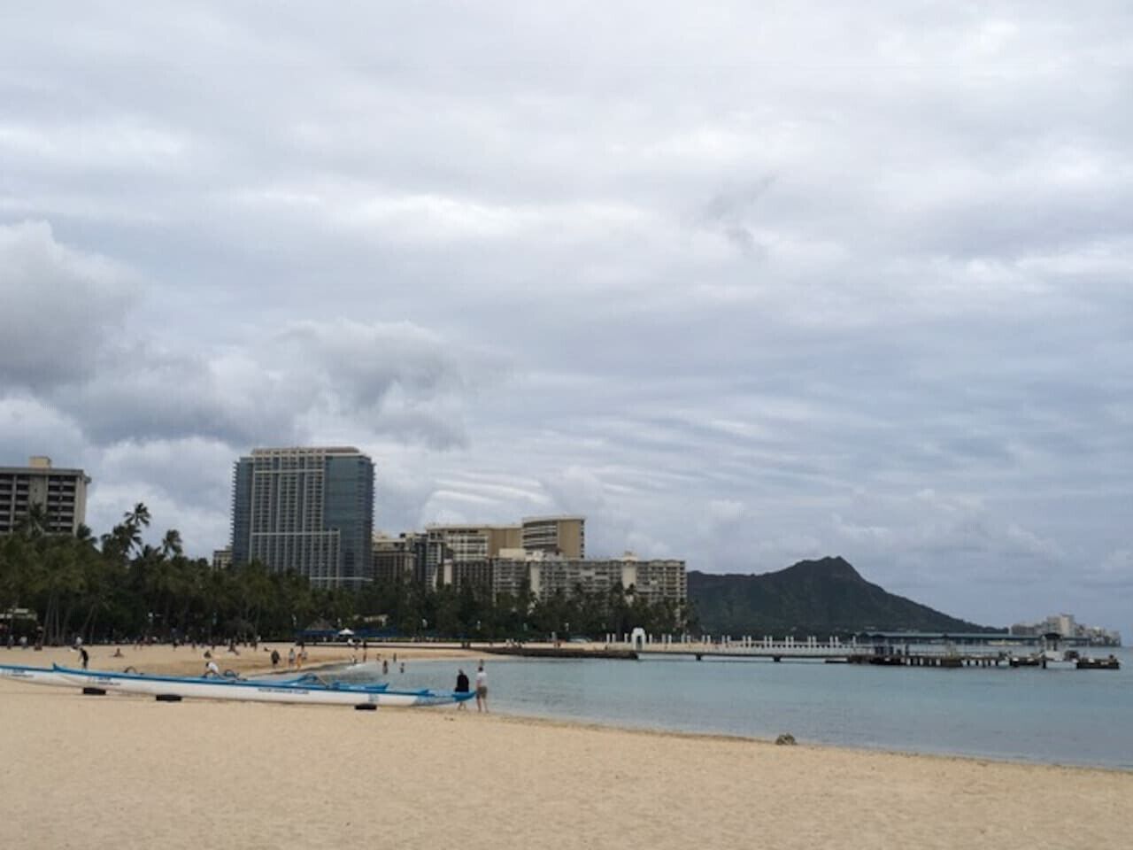 A beach with a row of boats, a pier, and buildings in the background.