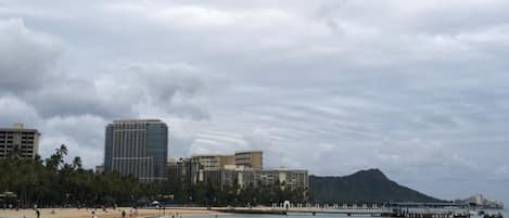 A beach with a row of boats, a pier, and buildings in the background.