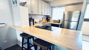 A modern kitchen with a wooden island, stainless steel appliances, and bar stools. - Waikiki 2 Bedroom w/ Covered Parking, Family Condo (Honolulu)