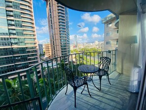 Een balkon met twee stoelen en een tafel, met uitzicht op een stadsbeeld met hoge gebouwen en een heldere lucht.