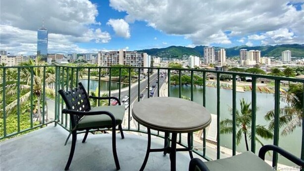 Un balcone con un tavolo e due sedie, vista su un fiume con uno skyline sullo sfondo.