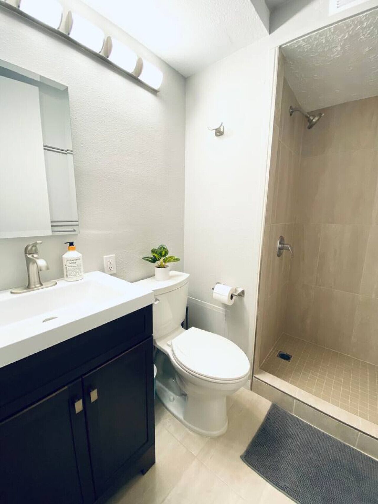 Une salle de bain moderne avec un lavabo blanc, des meubles sombres, des toilettes et une douche à parois de verre.