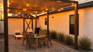 Une terrasse extérieure dot ée d’une pergola en bois, de guirlandes lumineuses, d’une table ronde et de chaises.