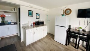 A compact kitchen with white cabinets, a microwave, and a refrigerator. There is a small dining table with two chairs and a clock on the wall. - Waikiki Clean Studio with Canal View (Honolulu)