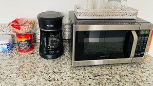 A kitchen counter with a stainless steel microwave, a coffee maker, a container of Folgers coffee, and a decorative tray with glasses. - Waikiki Clean Studio with Canal View (Honolulu)