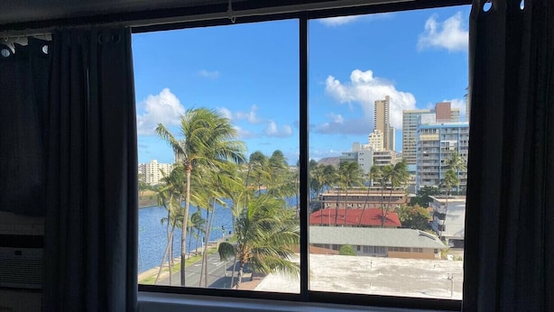 A hotel room with a large window offering a view of a beach and palm trees. - Waikiki Clean Studio with Canal View (Honolulu)