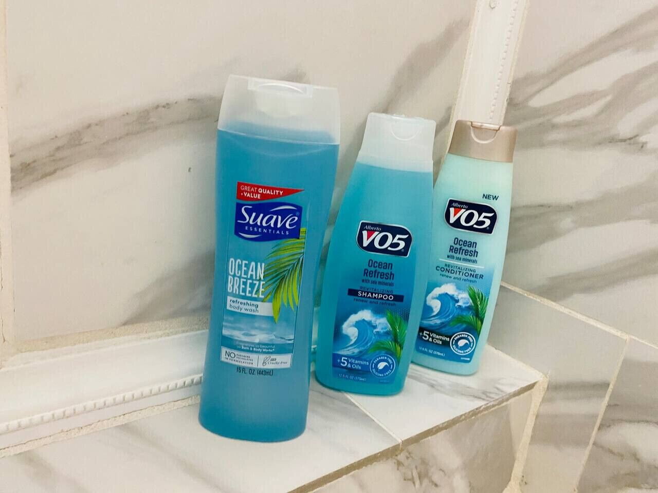 Tres botellas de jabón de baño sobre un estante de baldosas de mármol.