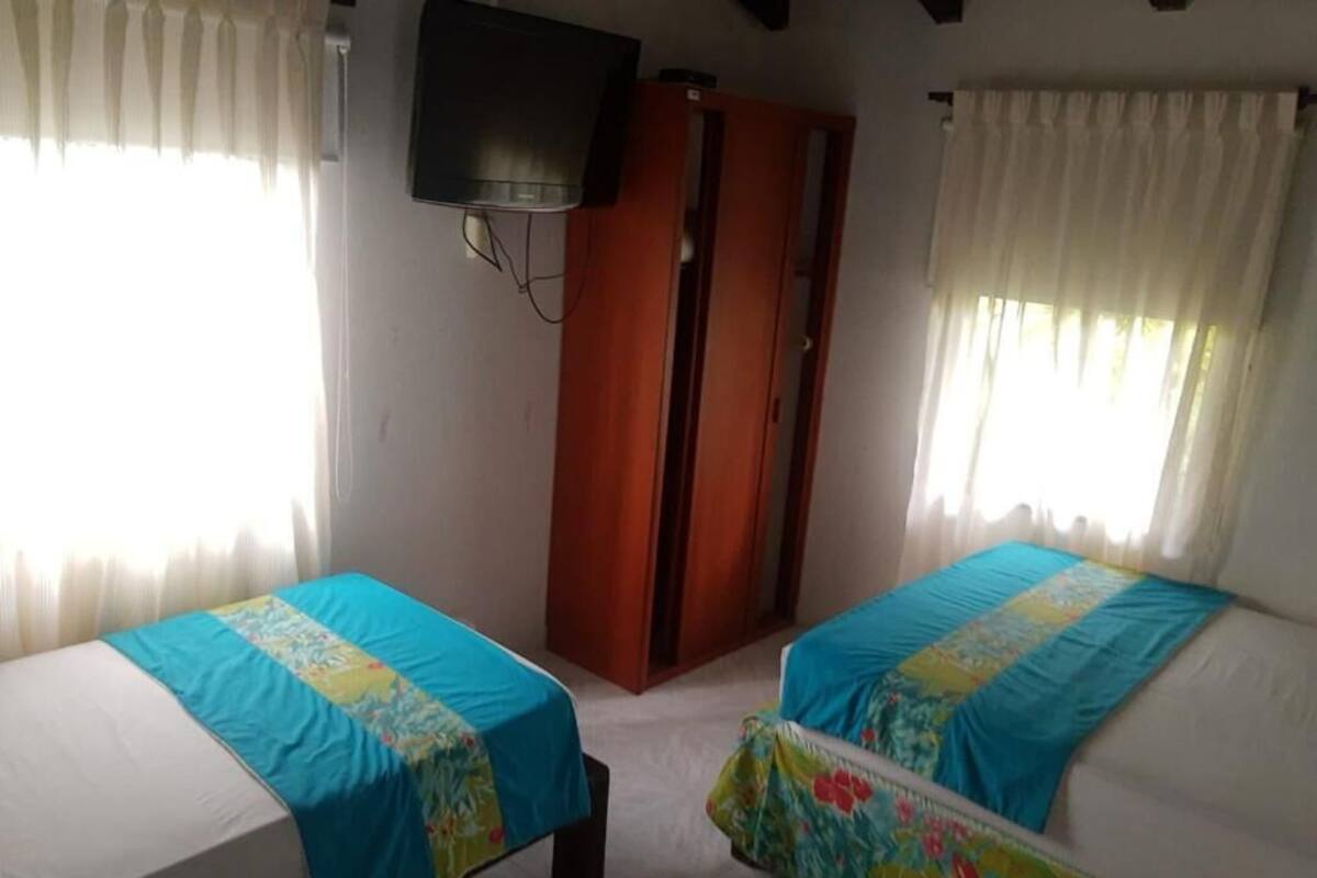 Una stanza con due letti, ognuno con una coperta blu, un armadio in legno e un televisore fissato al muro.