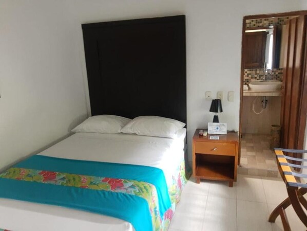A hotel room with a bed, a nightstand, a desk, and a bathroom with a sink and mirror. - Hotel San Antonio del Cerro (Pereira)