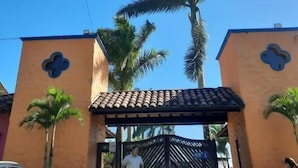 A building with a tiled roof entrance, palm trees, and a parked car. - Hotel San Antonio del Cerro (Pereira)