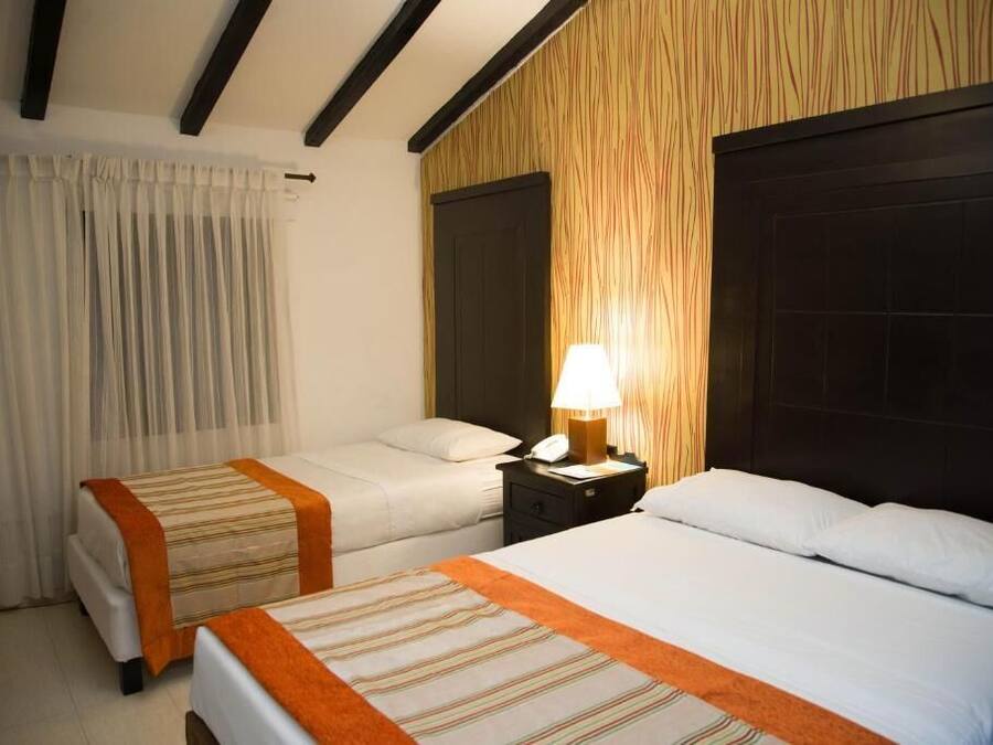 A hotel room with two beds, a nightstand with a lamp, and a wooden accent wall.