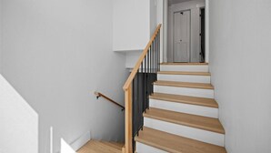 Eine Treppe mit hölzernen Stufen und einem schwarzen Geländer, die zu einer Tür oben führt.